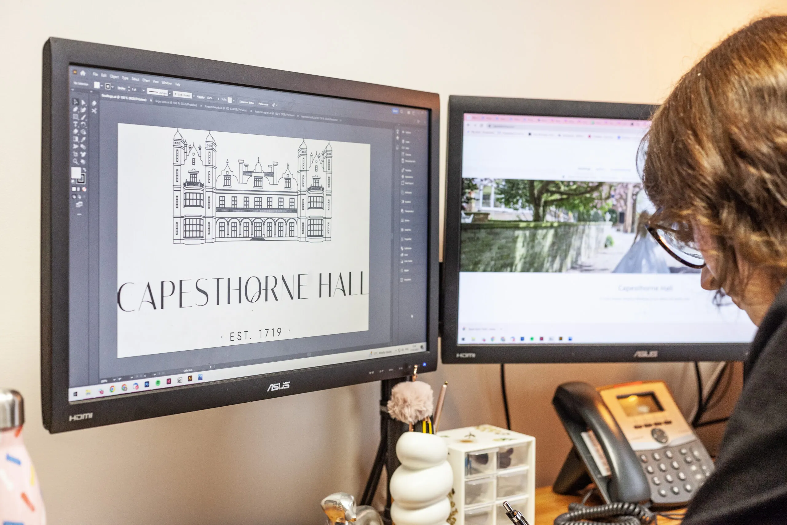 A woman at a desk with a computer drawing a logo design