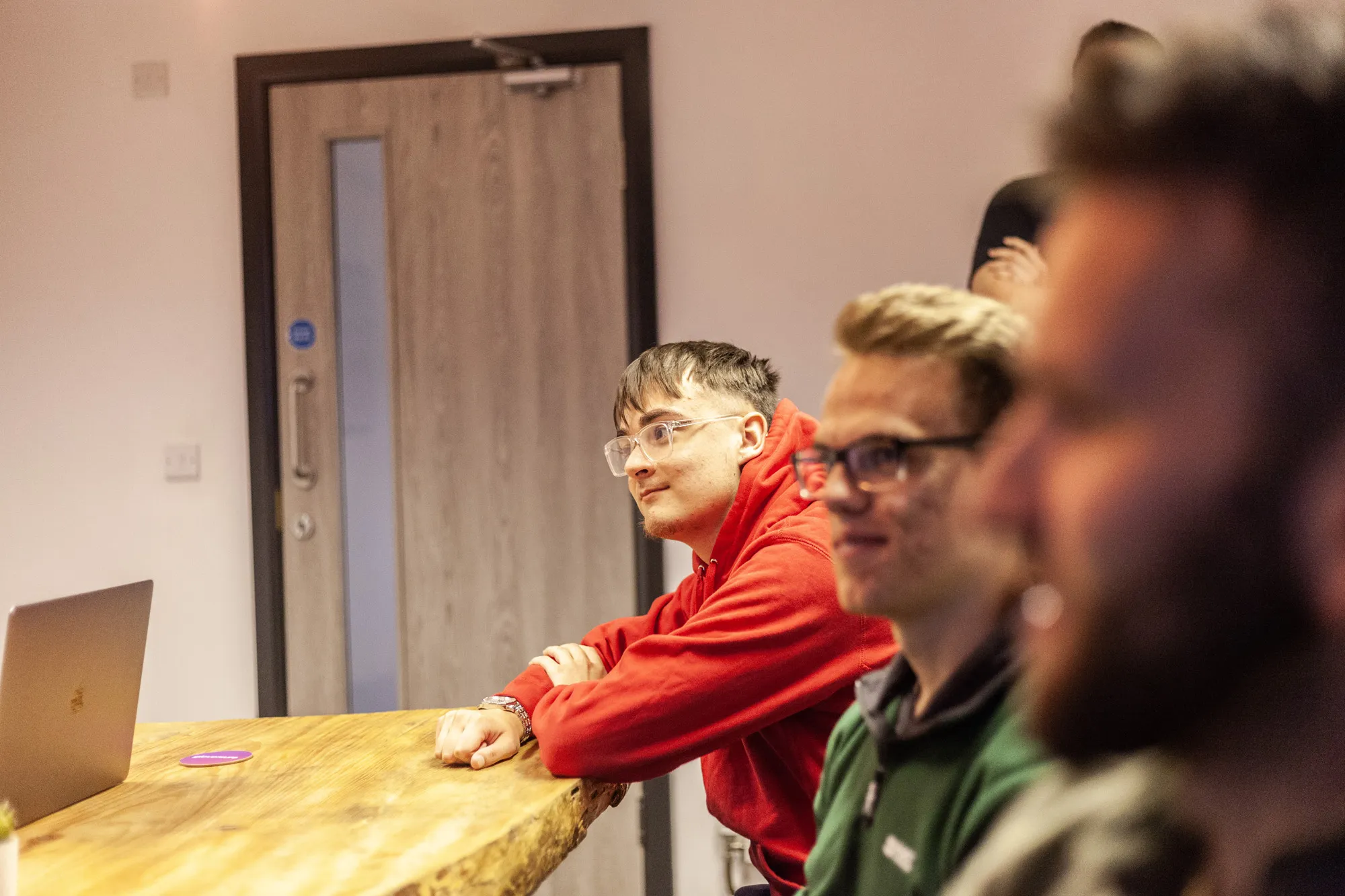 A group of men sat around a wooden table looking on