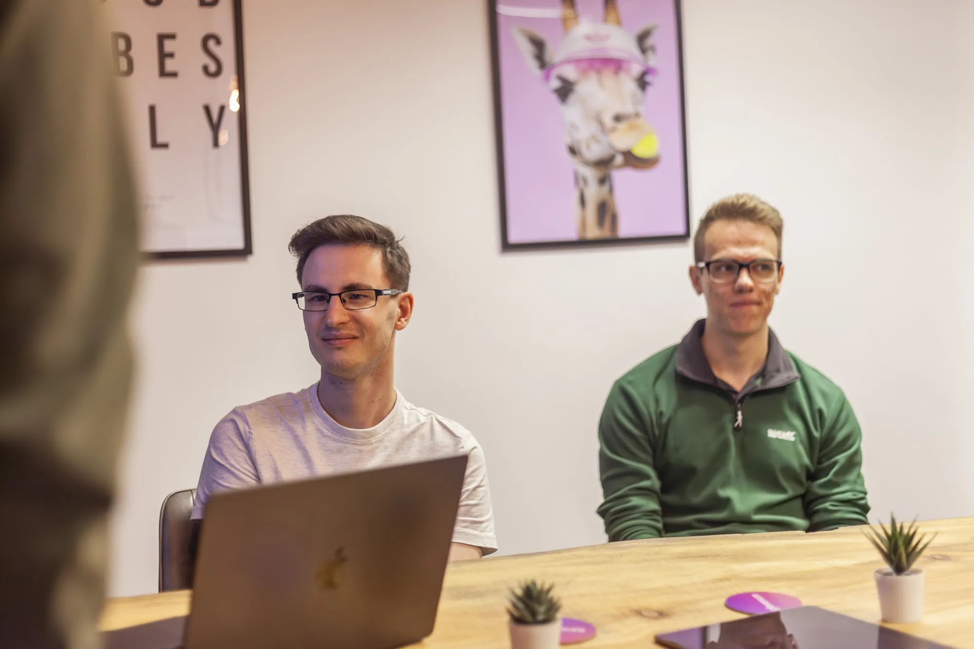 Two men sitting at a wooden table with a MacBook