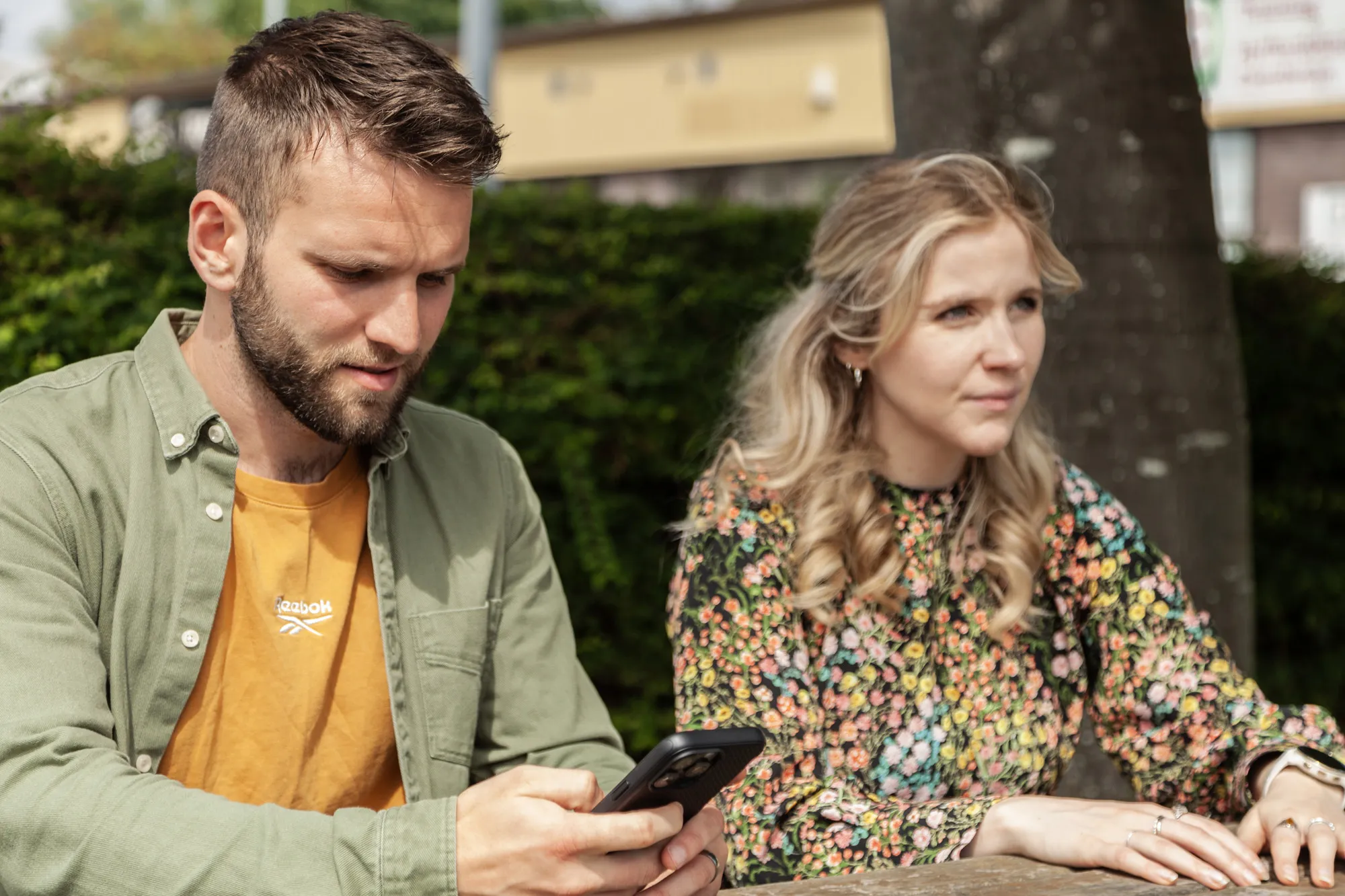 A man and a woman sitting on a wooden bench looking at an iPhone