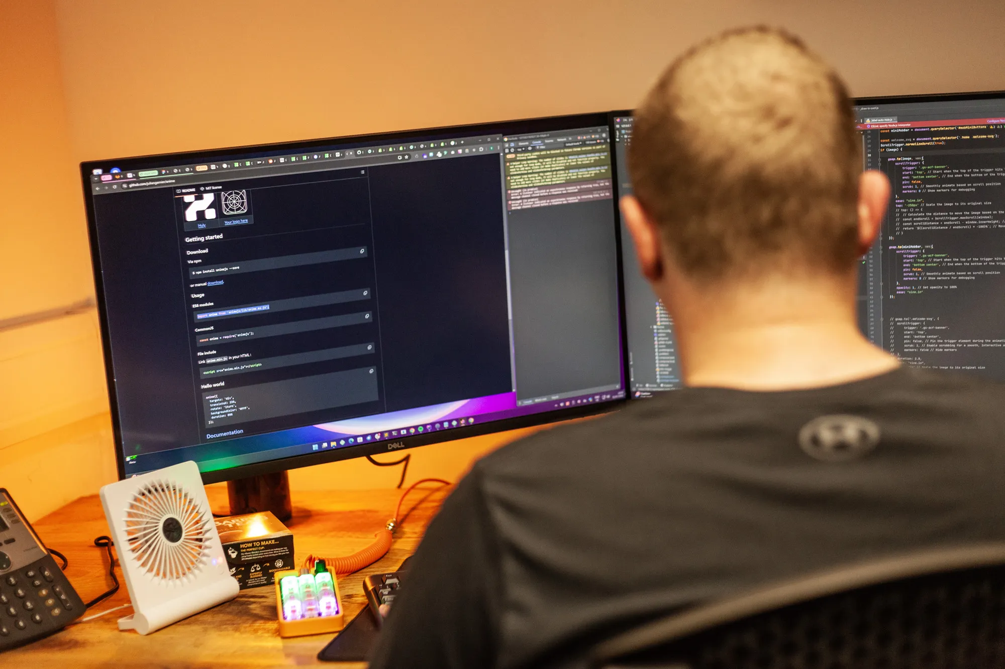A man sitting at a wooden desk looking at a computer screen with lines of code