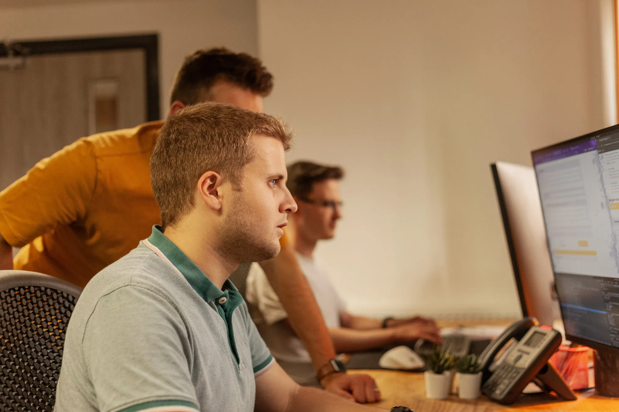 Three men in front of a desk looking at computers