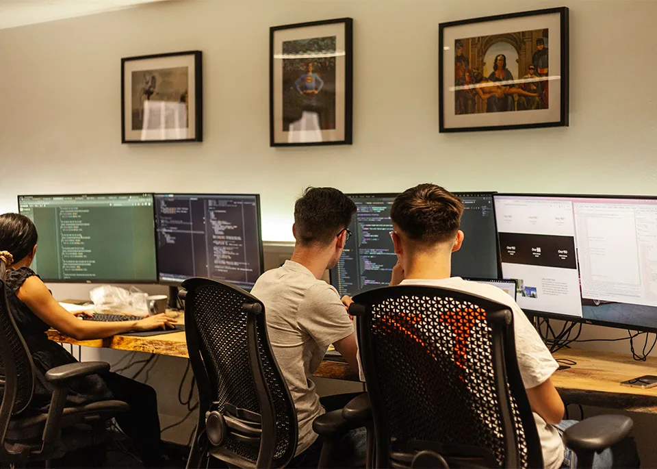 A group of people sat at a long desk with computers showing lines of code