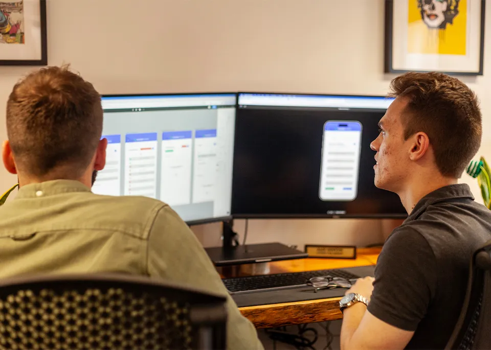 Two men sat in front of a computer screen showing mobile app prototypes