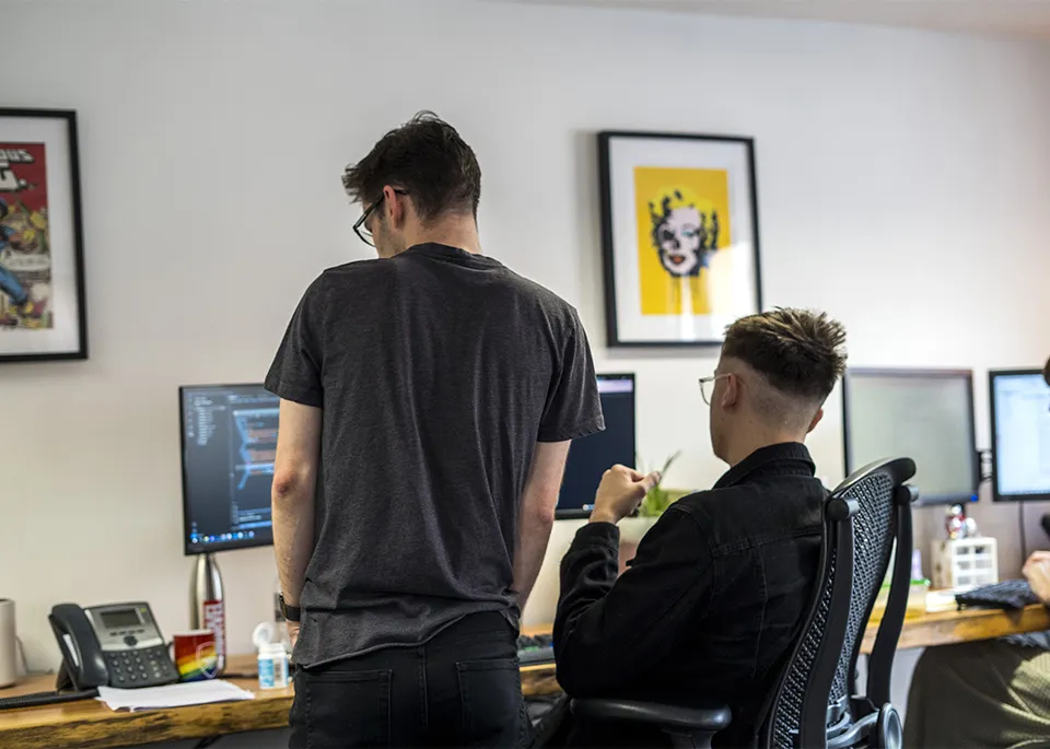 Two men at a desk looking at a computer screen with lines of code