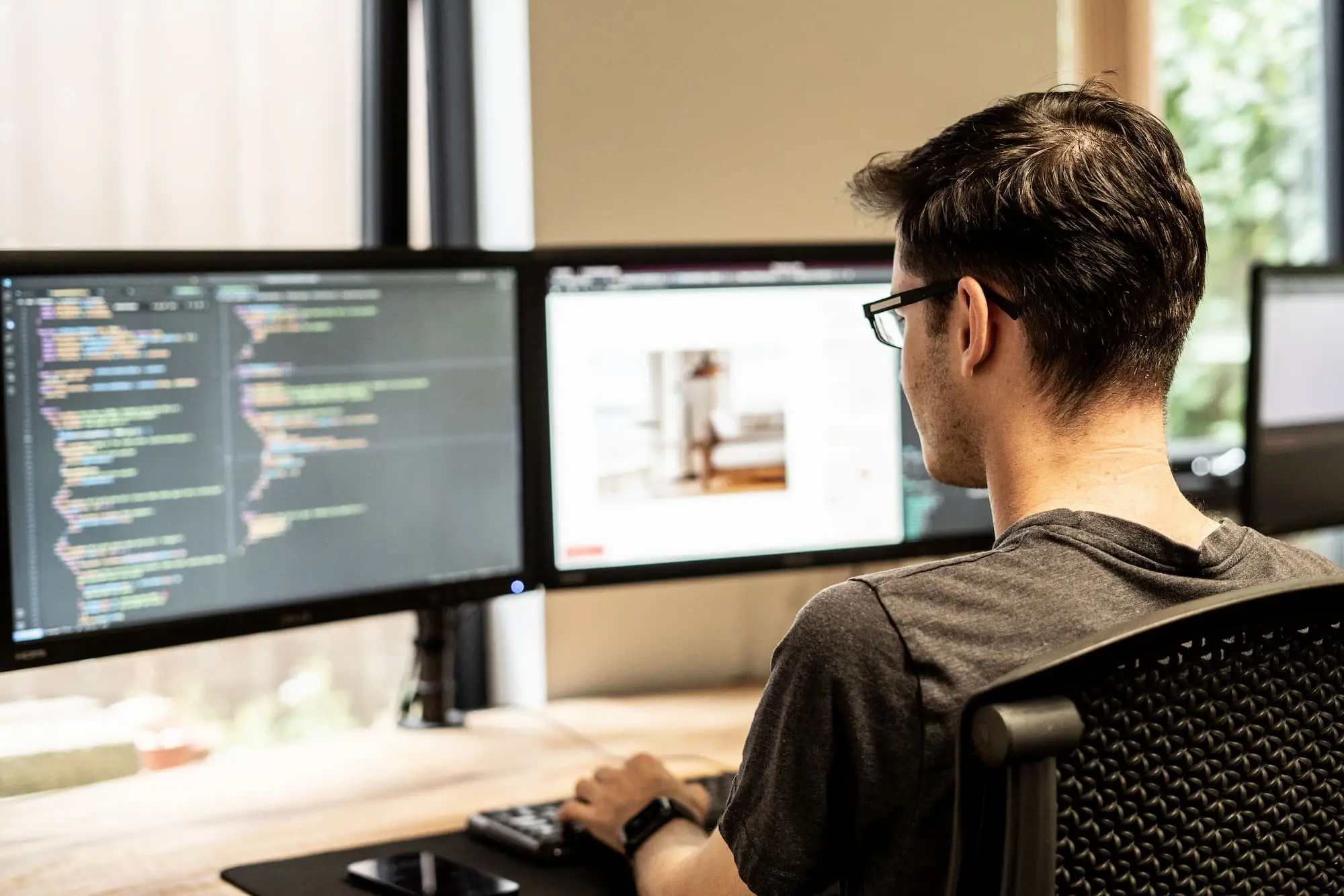 A man sitting at a desk looking at a computer screen showing lines of code
