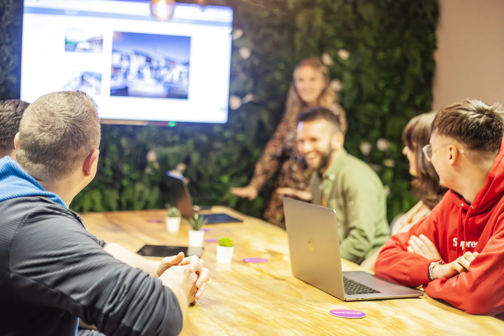 A group of people sat around a wooden table with a laptop smiling