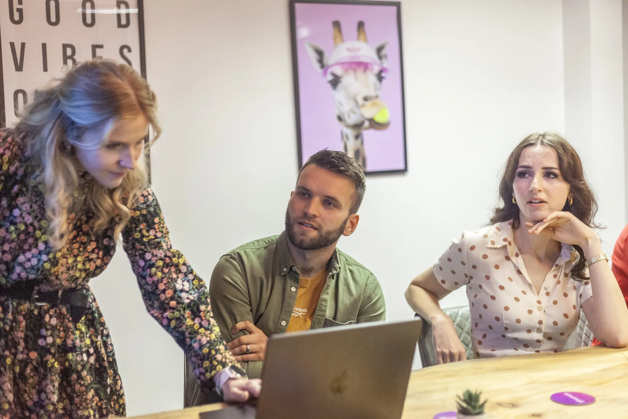 Two women and a man at a wooden table with a MacBook