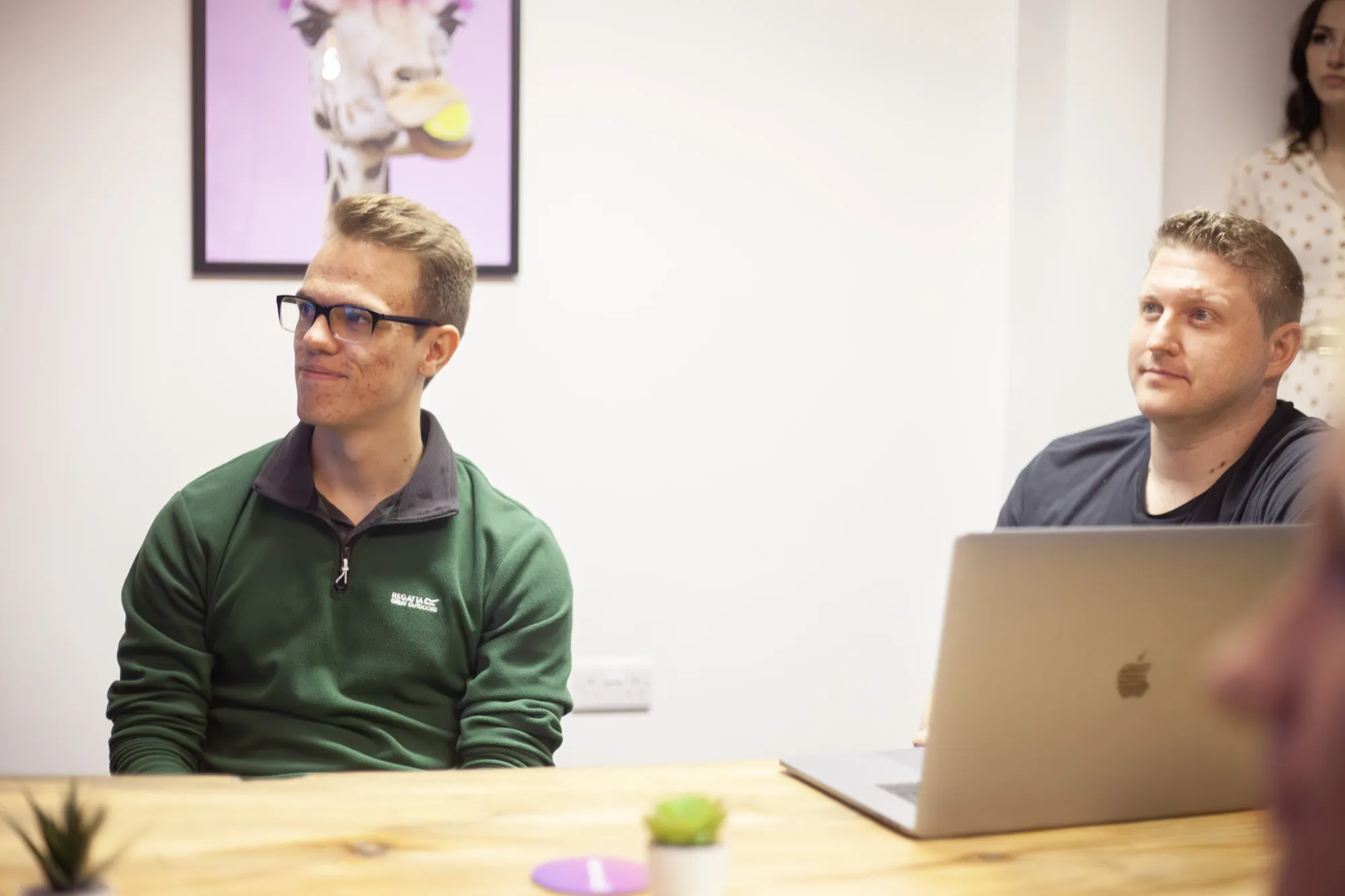 Two men sat at a wooden table in front of a laptop