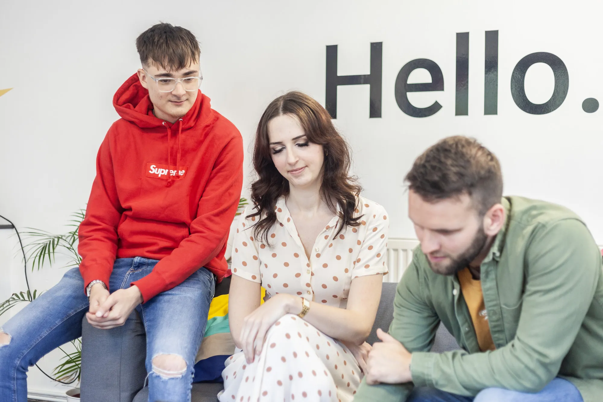 Two men and a woman sat on a grey sofa looking down at a MacBook