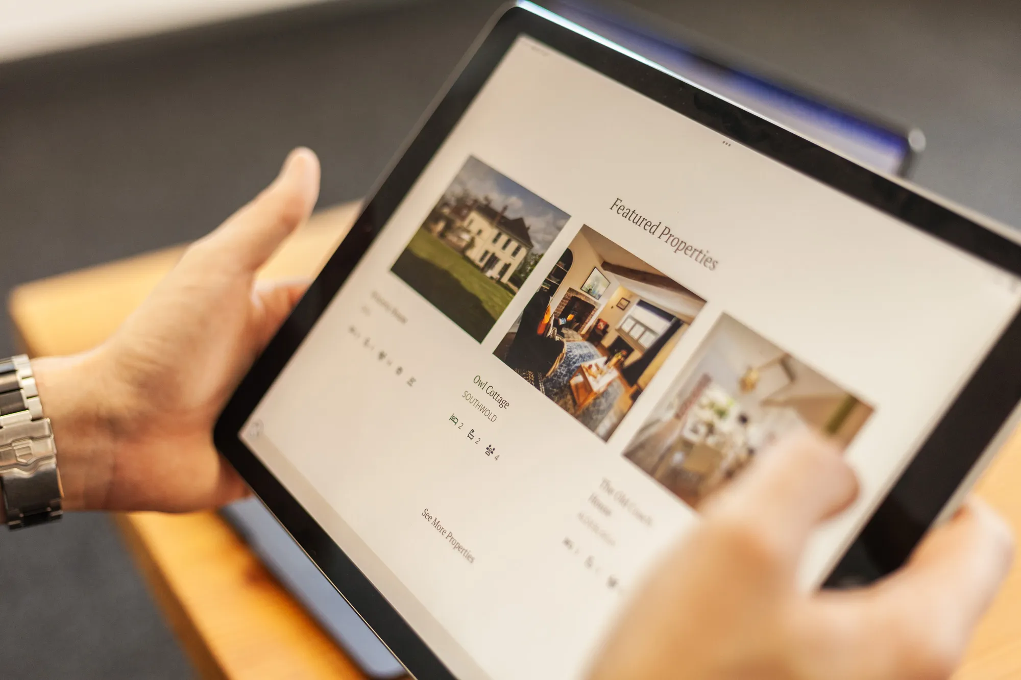 An iPad being held showing the Featured Properties section of the Curious Retreats website