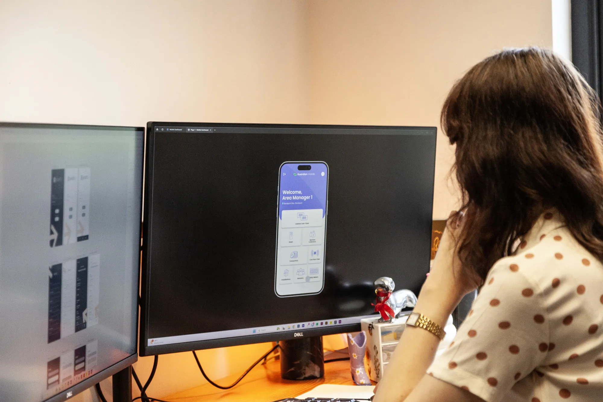 A woman sitting at a wooden table looking at a computer screen showing mobile app prototypes
