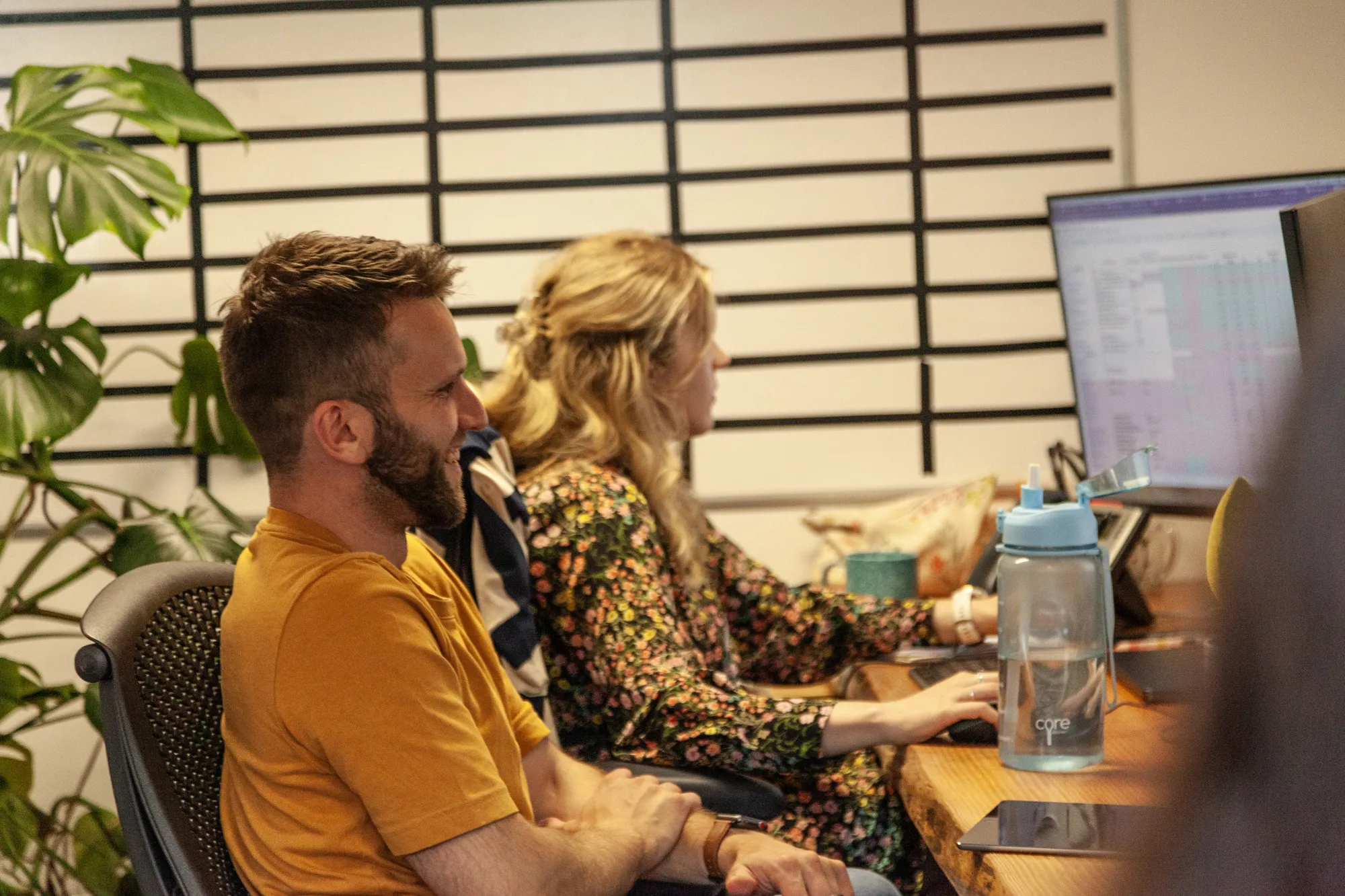 A man and a woman sitting at a wooden desk looking at computer screens