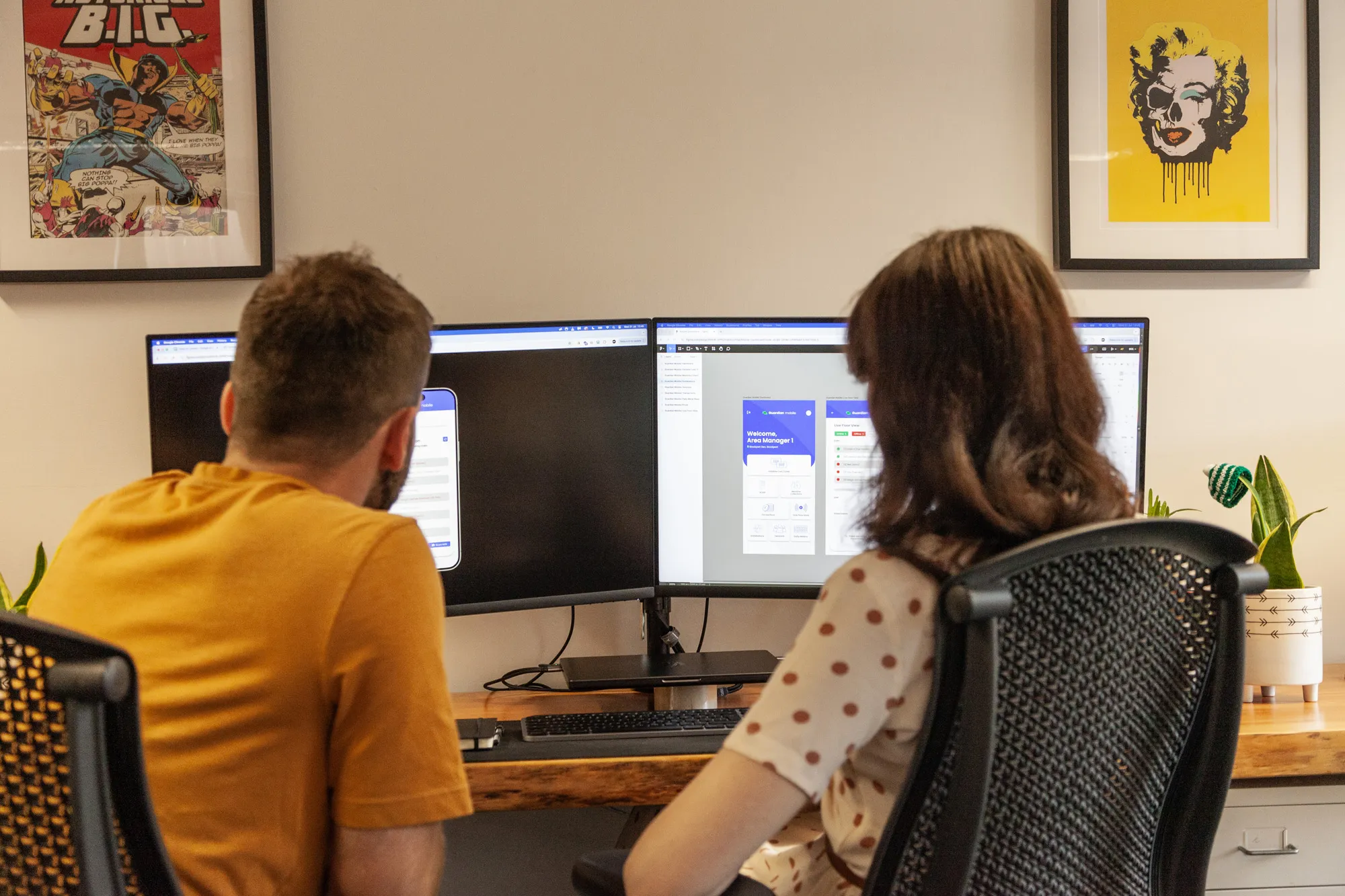 A man and woman sat at a wooden desk looking at computer screens
