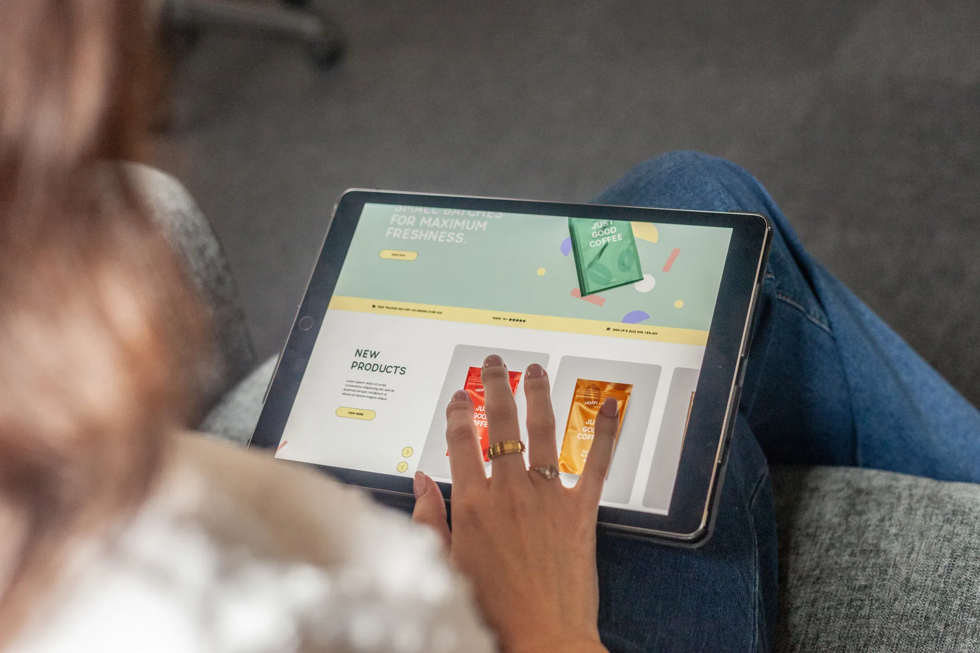 A woman sitting on a grey sofa using an iPad showing an eCommerce website for a coffee company