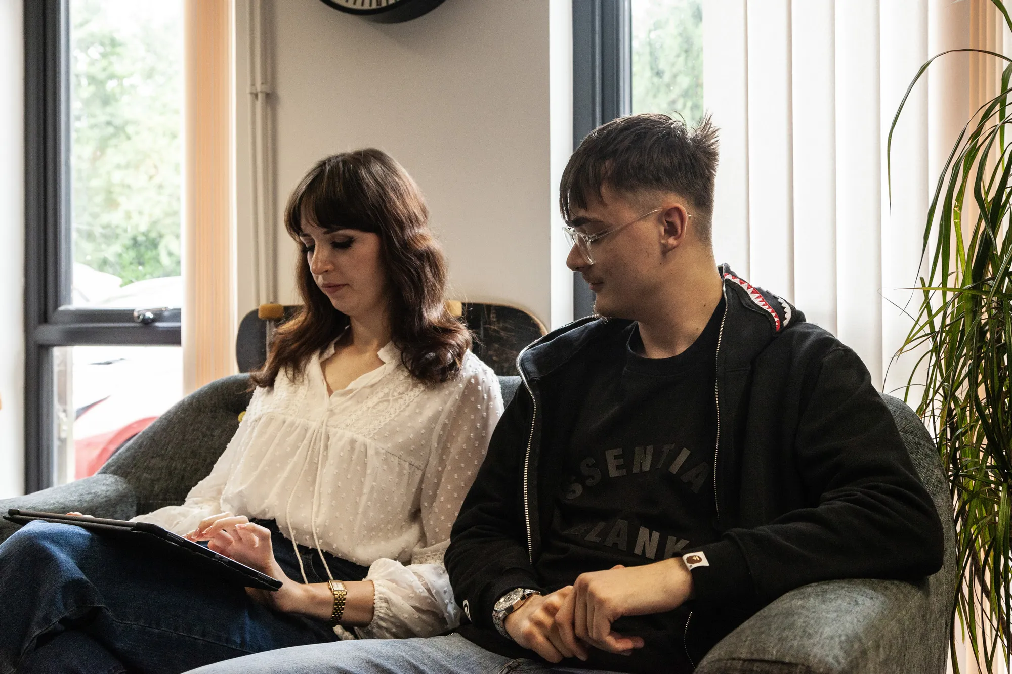 A man and a woman sat on a grey sofa looking down at an iPad