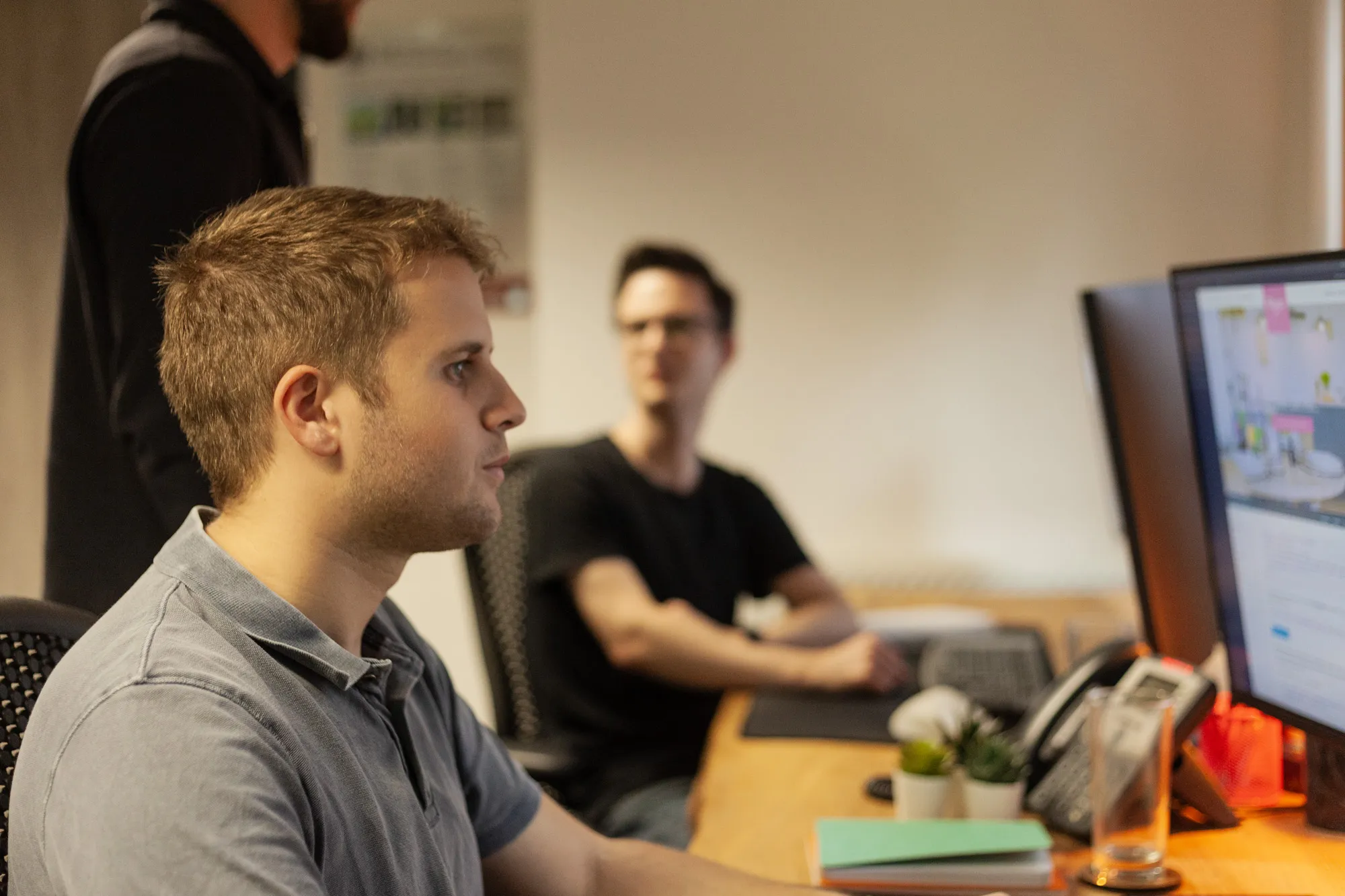 A man sitting at a desk in a busy office looking at a computer screen