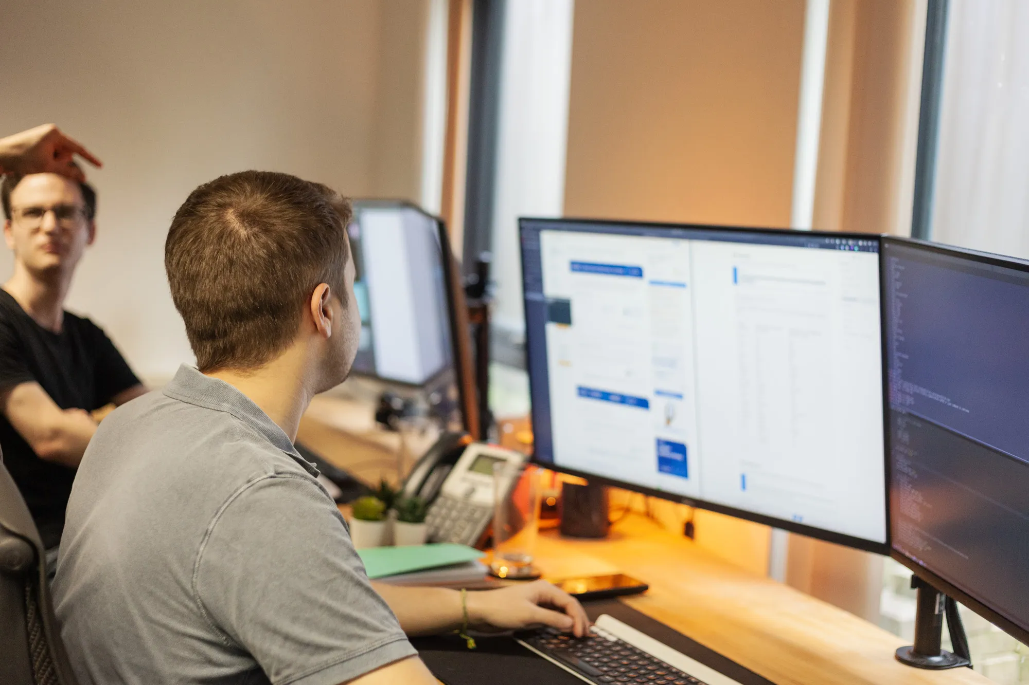 A man sitting at a desk looking at a computer with two screens
