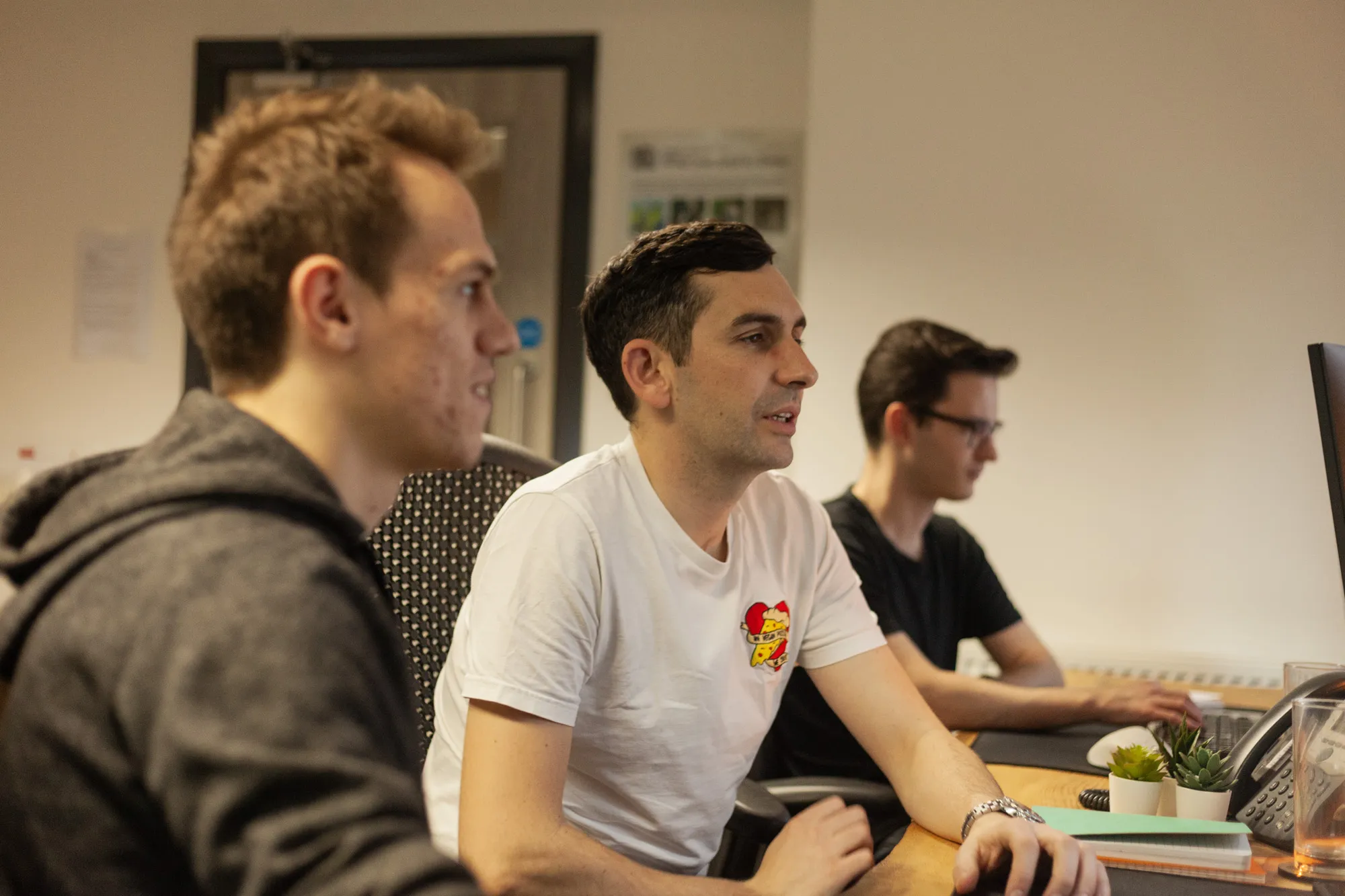 Three men sat at a desk looking at a computer