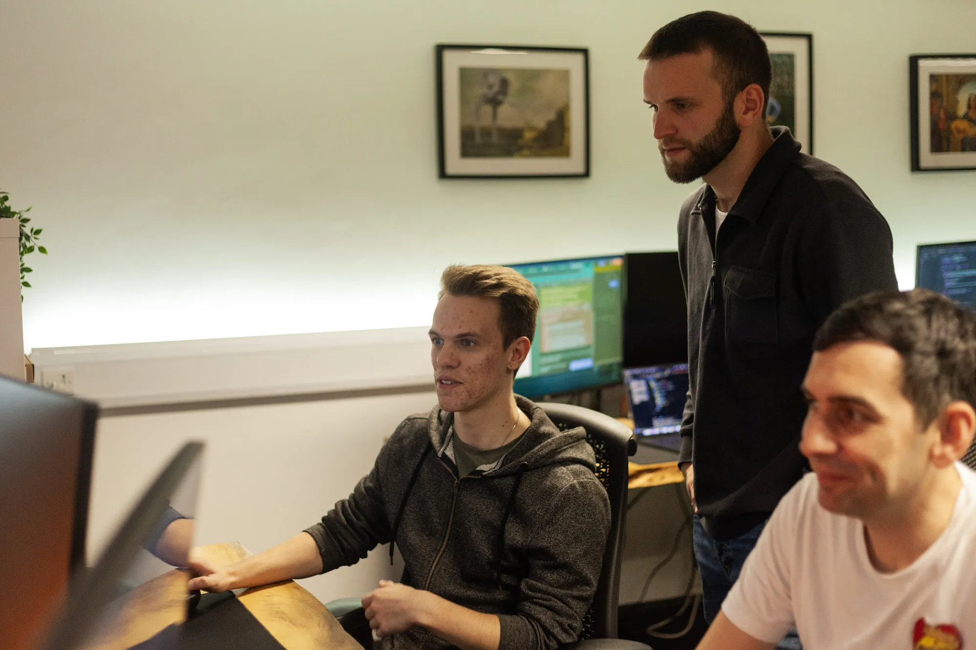 Three men sat at a desk looking at a computer