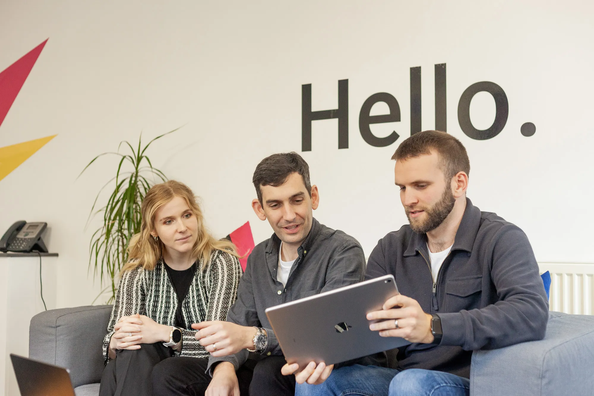 Two men and a woman sat looking at an iPad