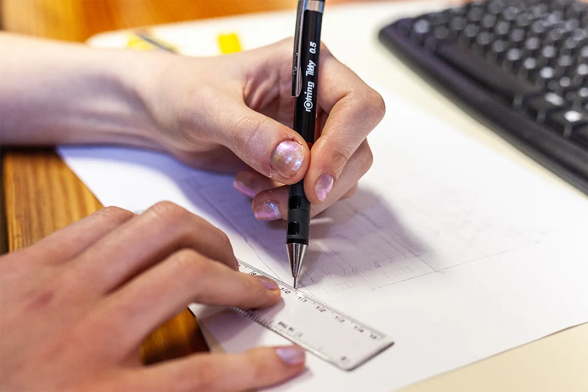 A woman using a pencil and ruler to draw a logo