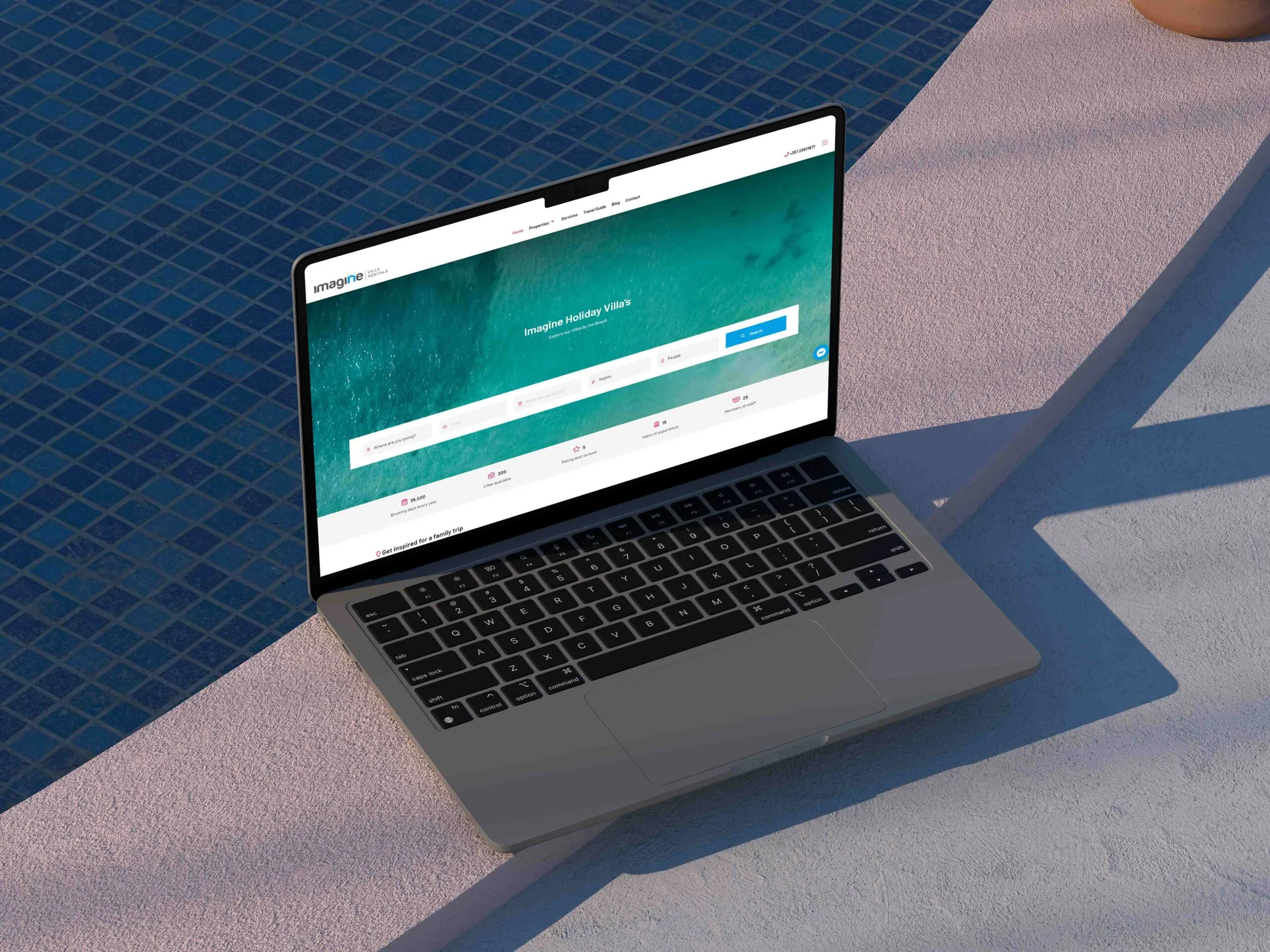 A MacBook by the edge of a swimming pool showing the Imagine Villas website homepage