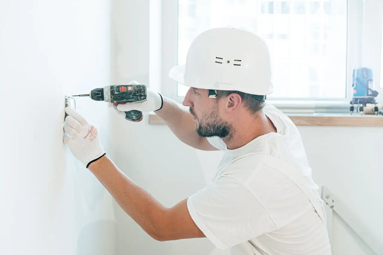 A man wearing a white hat drilling into a wall