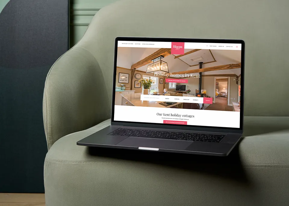 A MacBook on a green sofa showing the Bloom Stays website homepage