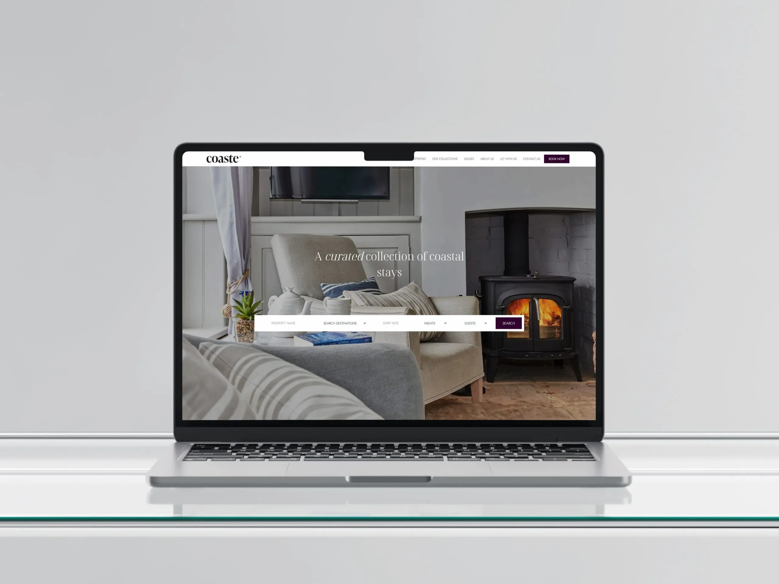 A MacBook on a glass table showing the Coaste website homepage