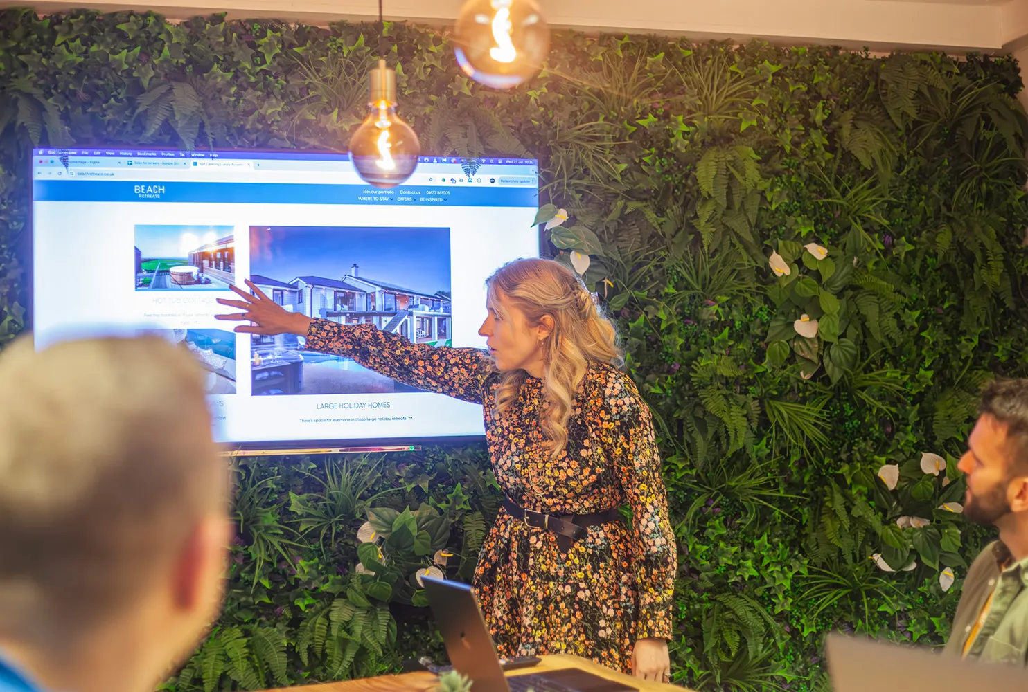 A woman pointing to a wall mounted TV screen in a meeting room