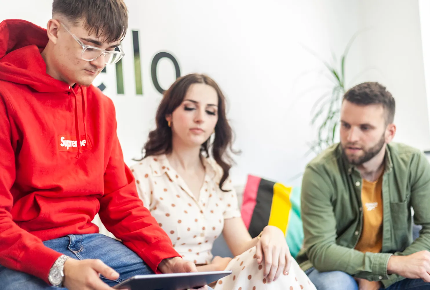Two men and a woman sat on a grey sofa looking down at an iPad