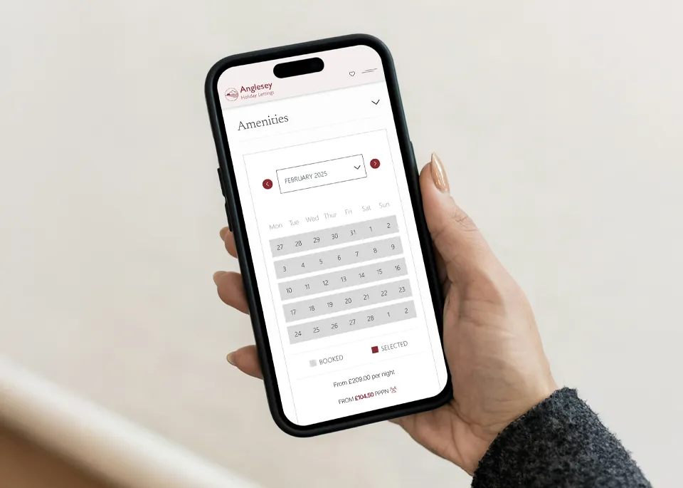 A person holding an iPhone showing the Anglesey Holiday Lettings property booking calendar