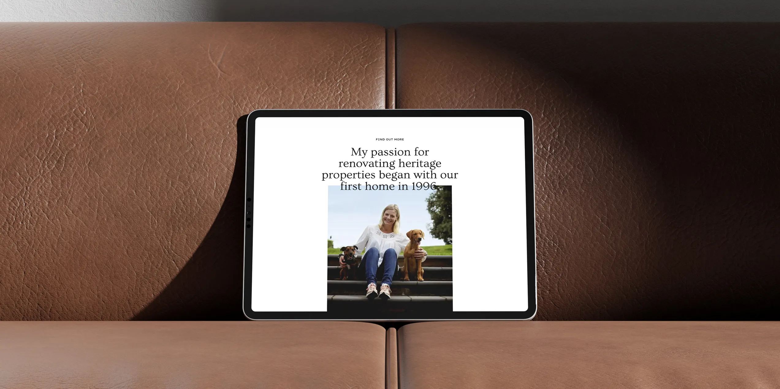 An iPad on a brown leather couch showing the Obstgarten Homes about us section on screen
