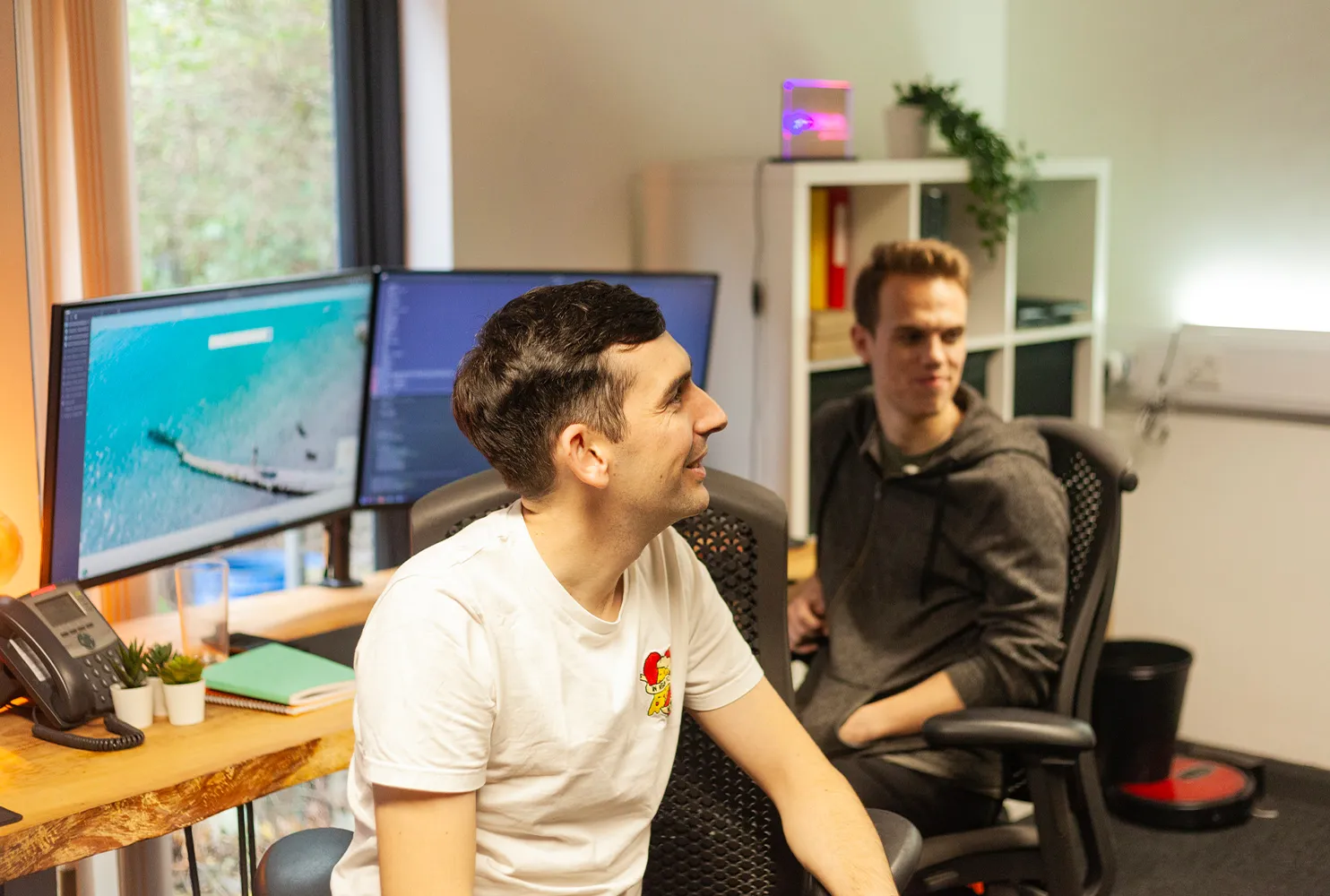 Two men sitting at a wooden desk smiling