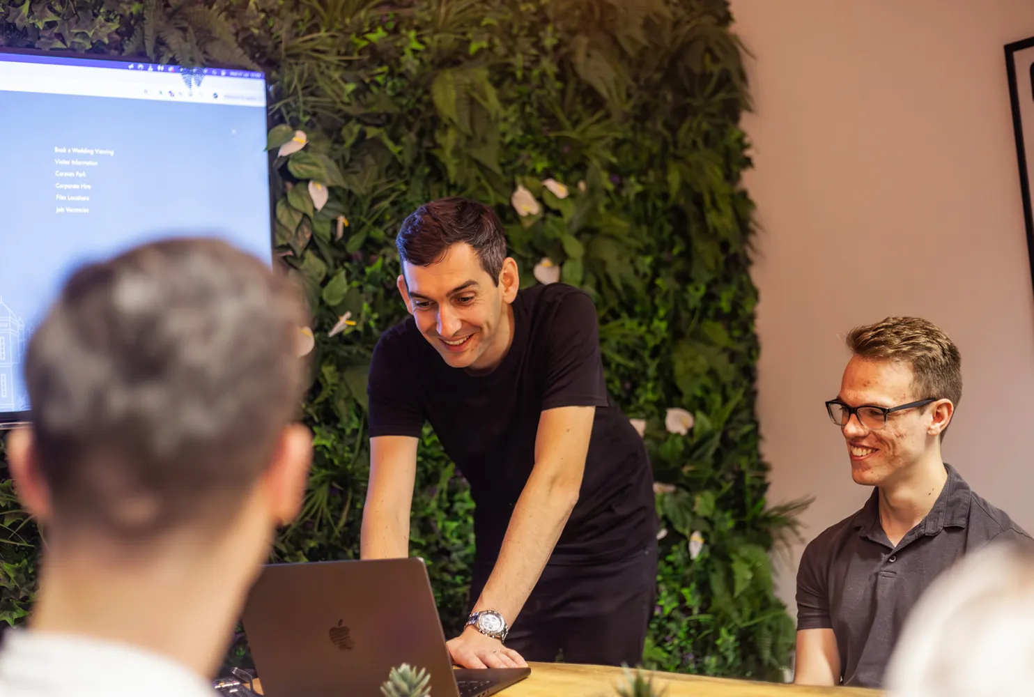 A man standing over a table using a laptop in a meeting room