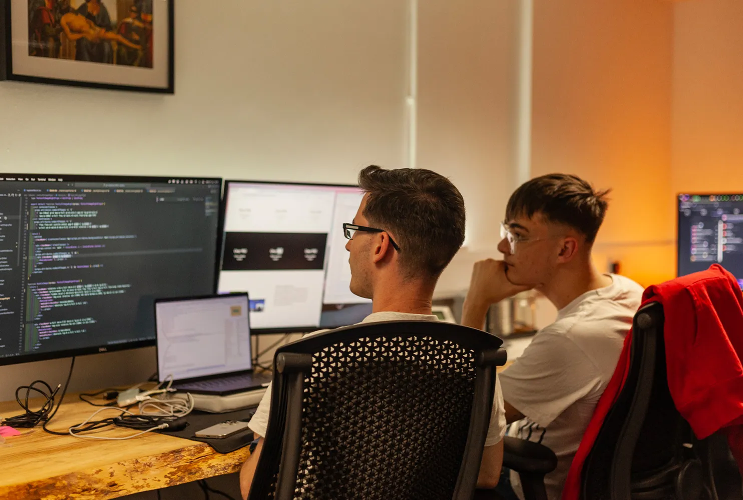 Two men sat at a desk looking at a computer showing lines of code