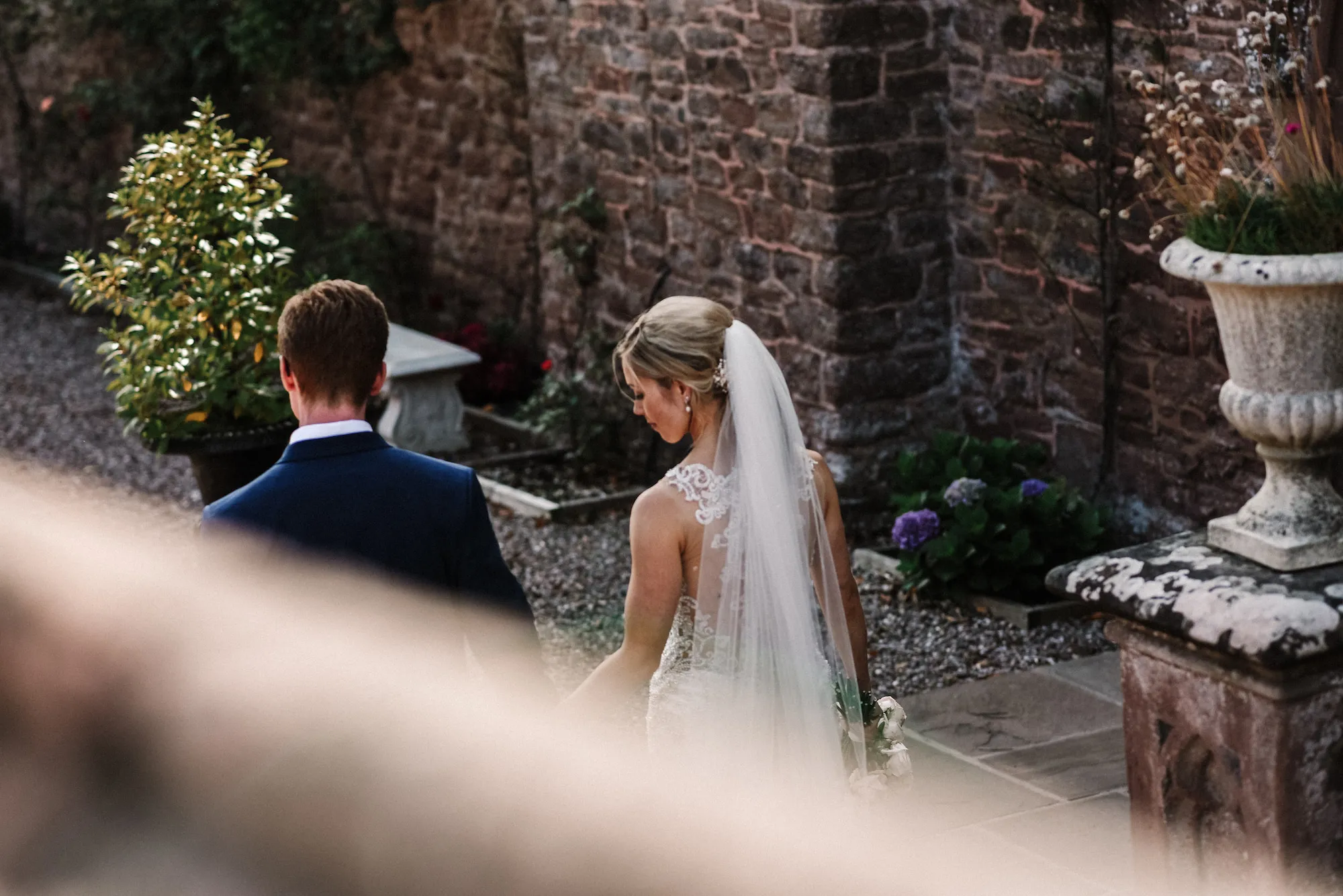 A man and a woman in formal wedding attire walking in a walled garden