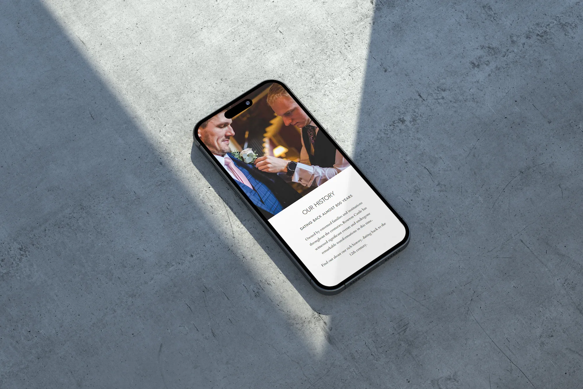 An iPhone on a grey concrete background showing the Rowton Castle history page