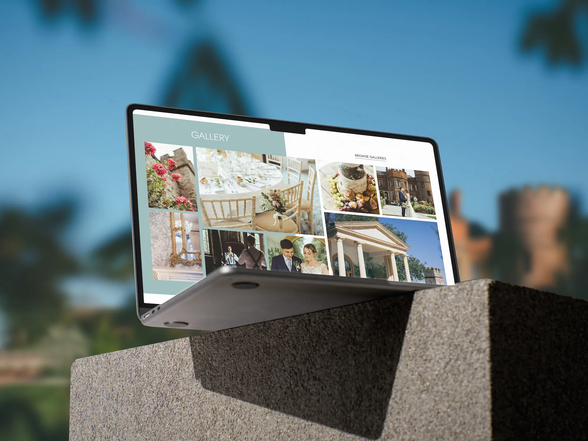A MacBook on a concrete block on the grounds of a large castle showing the Rowton Castle gallery section on screen