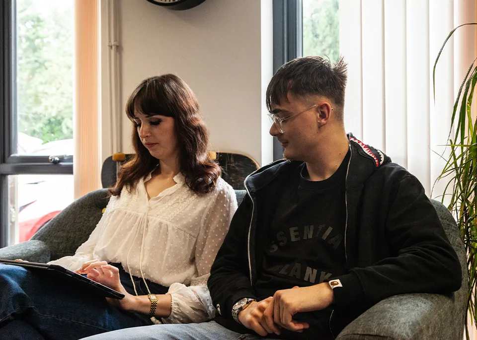 A woman and a man sitting on a couch looking down at an iPad
