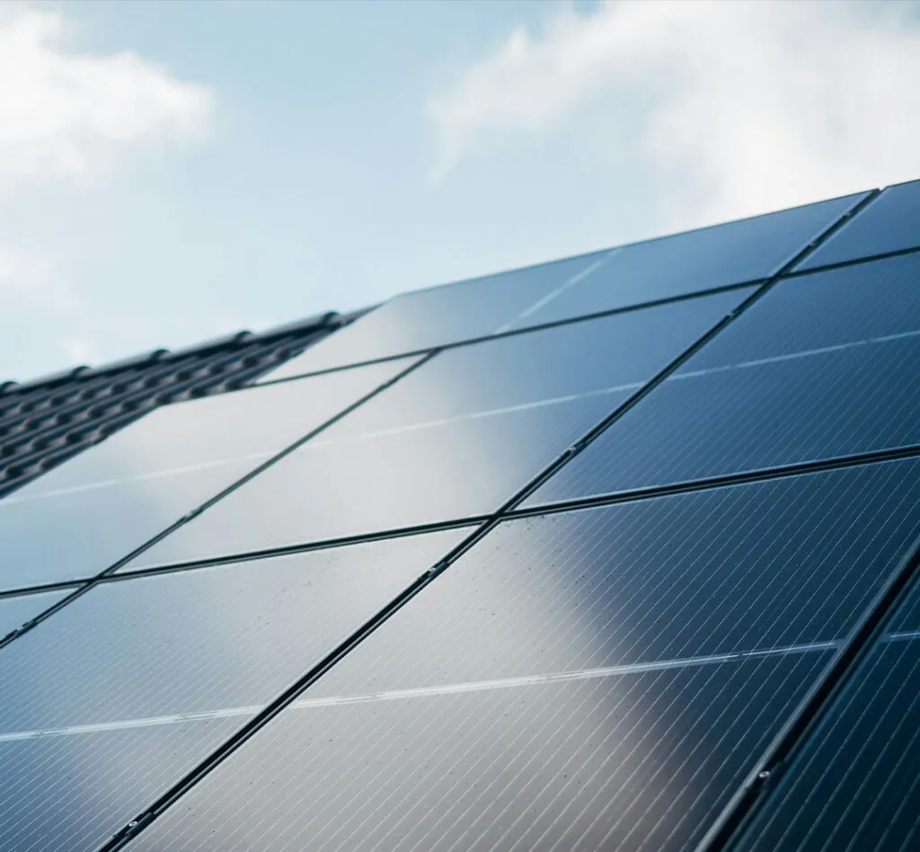 A close-up of solar panels on a roof under a clear blue sky reflecting sunlight