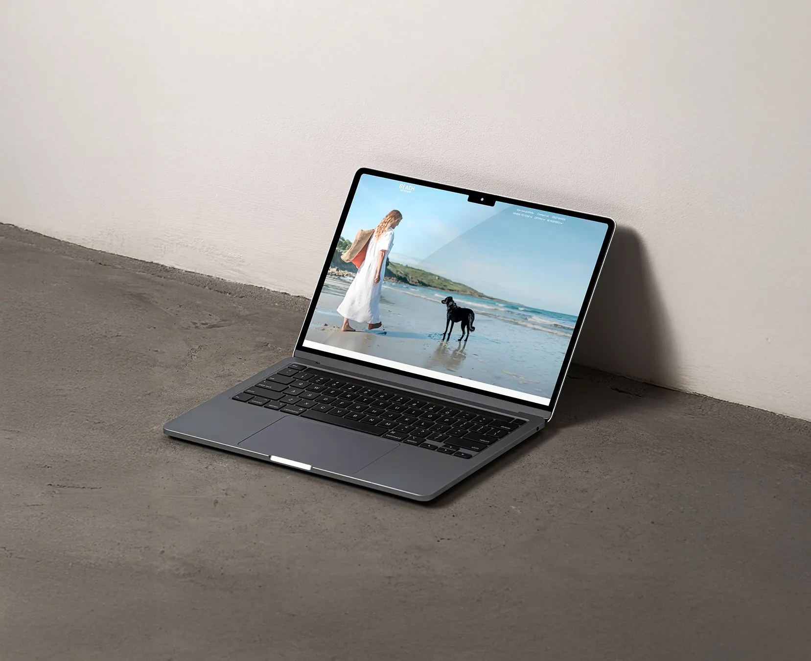 A MacBook sitting on a concrete floor angled against a wall showing the Beach Retreats website homepage