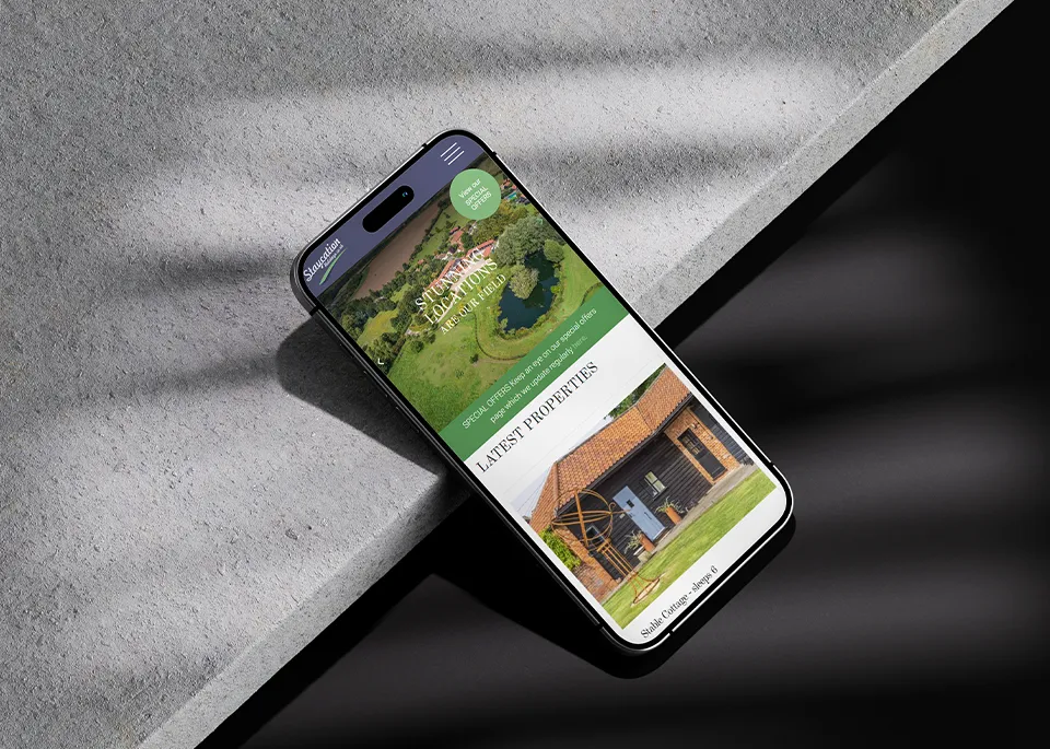 Smartphone displaying the Staycation Holidays website with property images resting on a textured grey surface