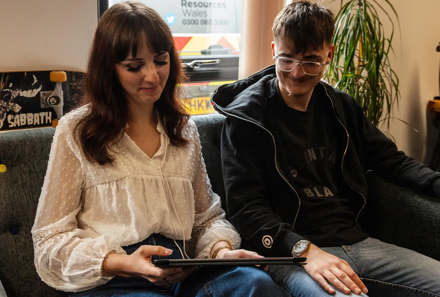 A woman and man sit on a couch, smiling while looking at a tablet