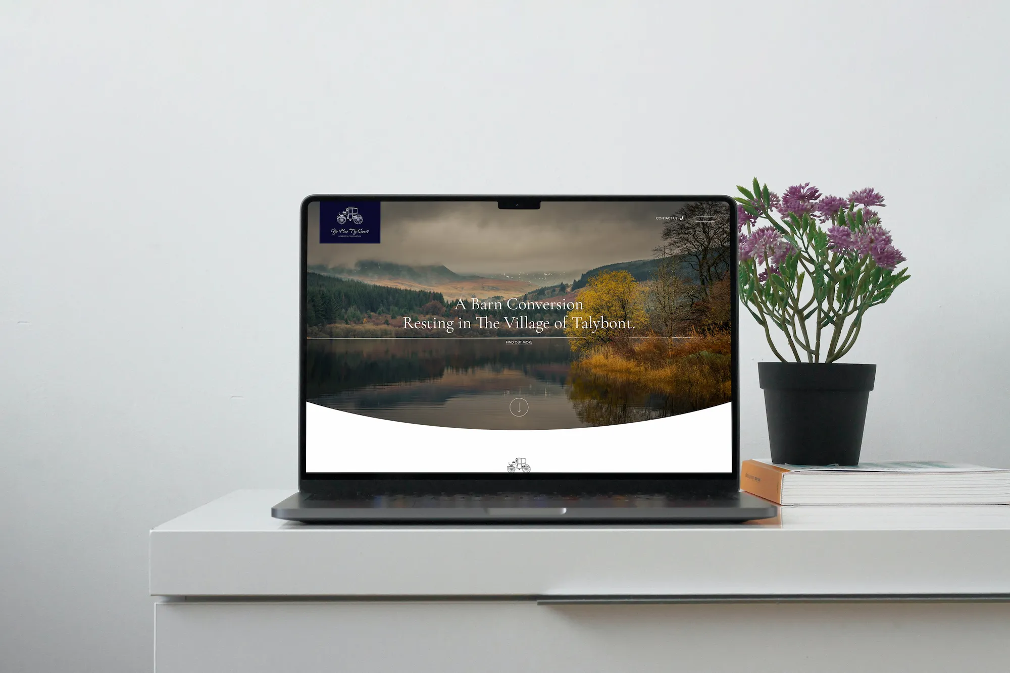 A laptop on a white desk showing the Yr Hen Ty Coets website homepage on screen