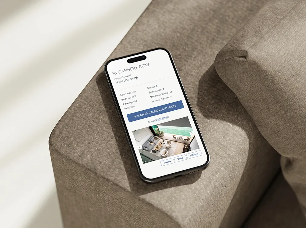 An iPhone on a beige couch displaying the Beach Retreats website with a property page titled 