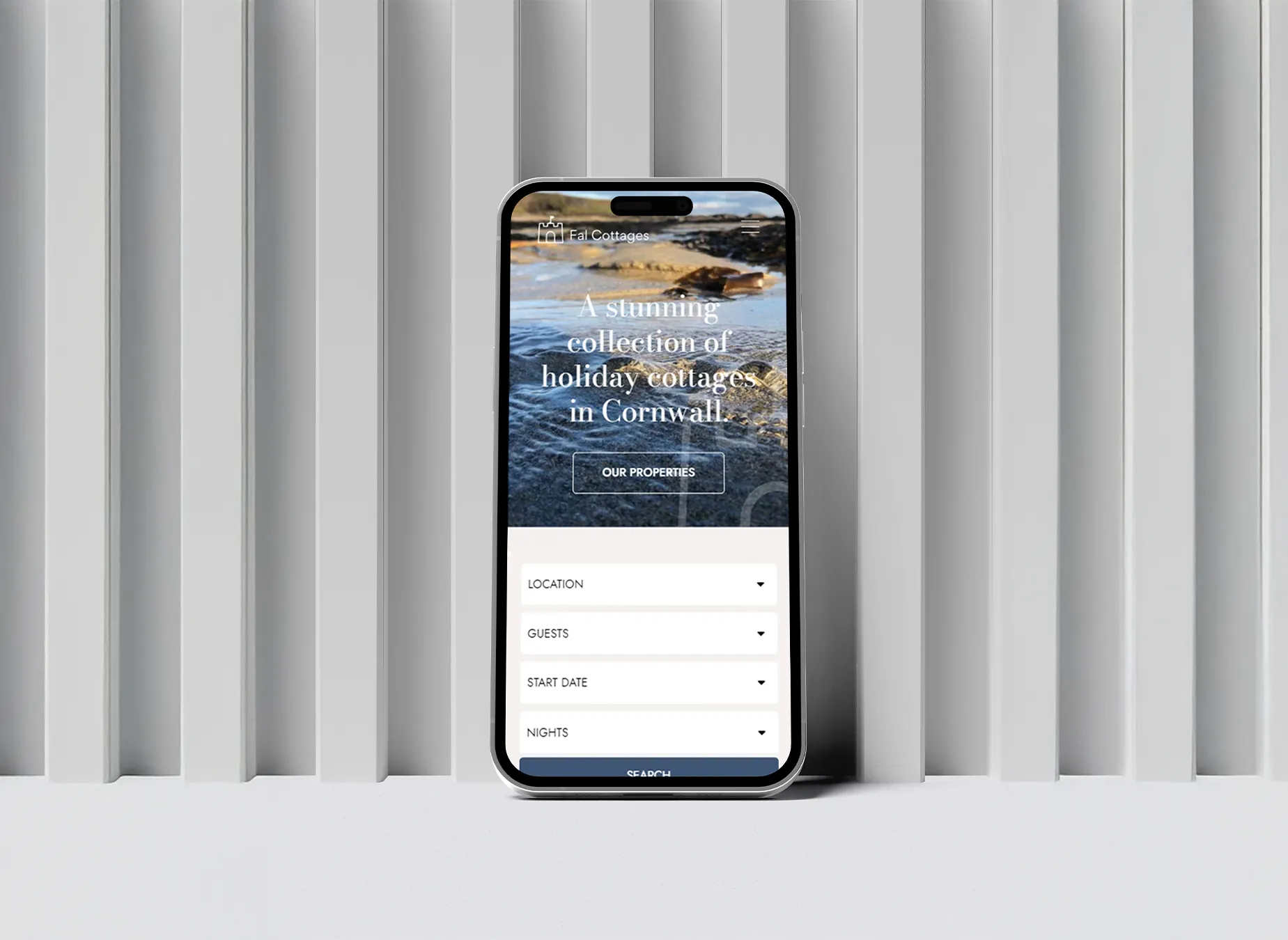 An iPhone displaying the Fal Cottages homepage standing against a textured grey wall