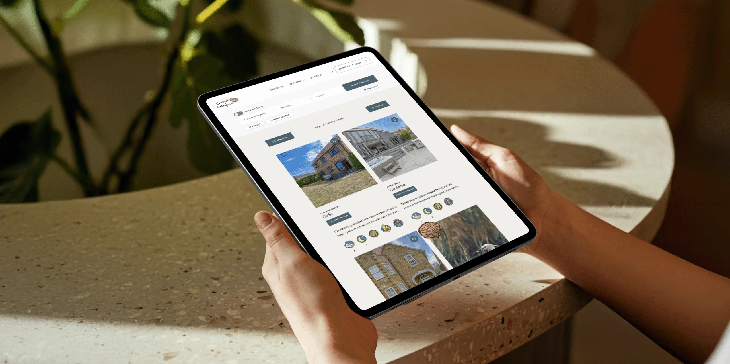 Hands holding a tablet displaying the Crabpot Cottages website property search page.