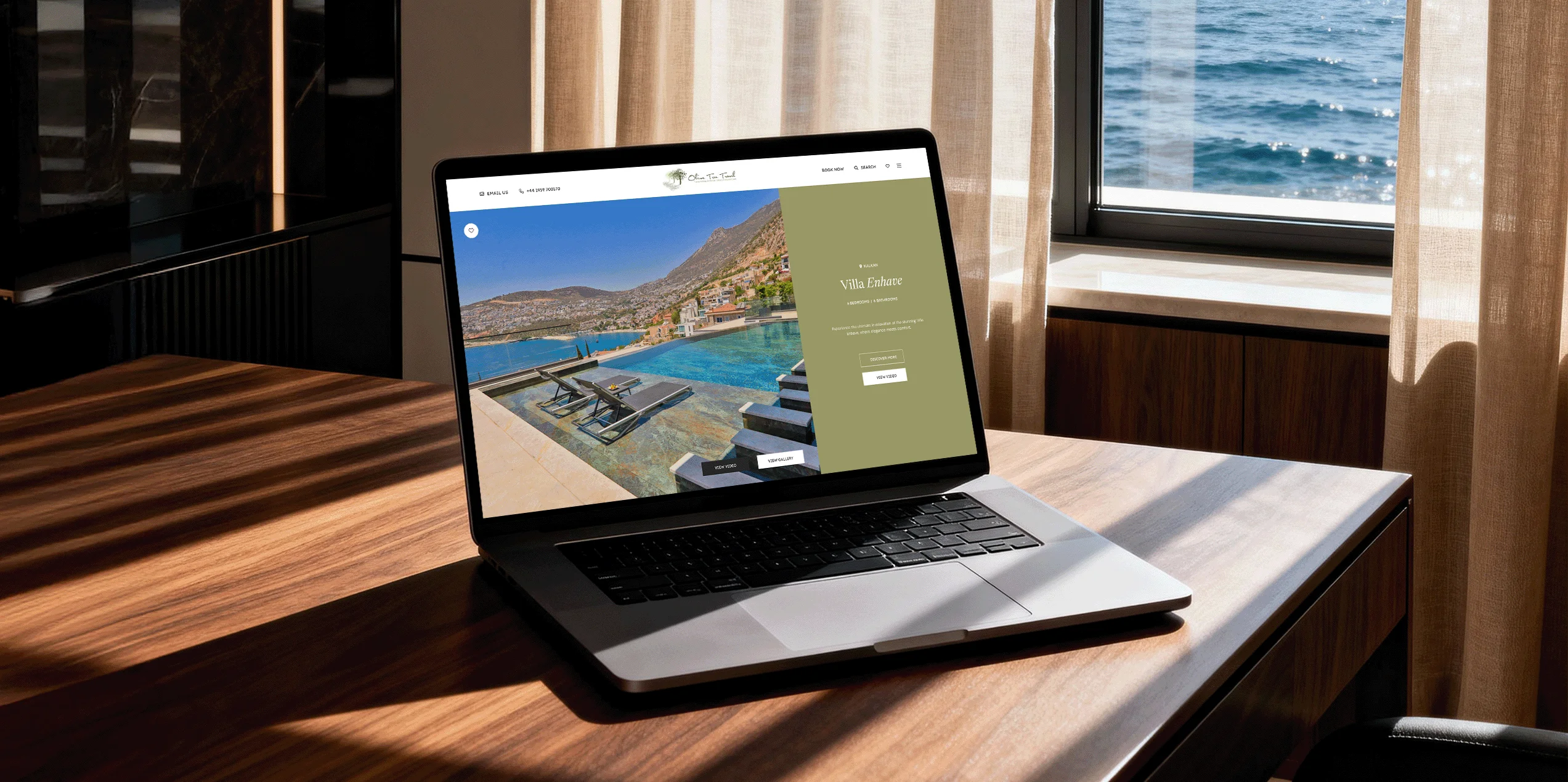 A laptop on a wooden desk by a window displaying the Olive Tree Travel website with an ocean view.